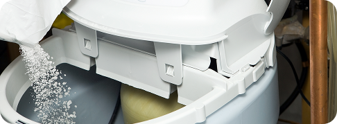 someone pours salt into a water softener unit