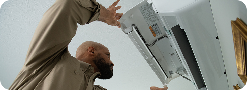 someone opens the cover of a ductless hvac unit on a wall