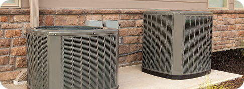 two outdoor heat pump units against a stone brick wall