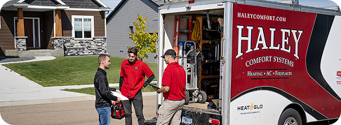 Haley Comfort Systems team members standing beside a service truck, discussing work outside a residential home.