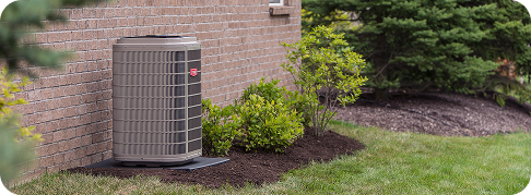 a grey air conditioning unit in a yard next to an exterior brick wall