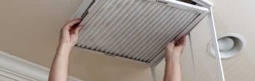 Senior male reaching up to open filter holder for an HVAC filter in the ceiling