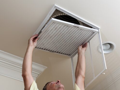 Senior male reaching up to open filter holder for an HVAC filter in the ceiling